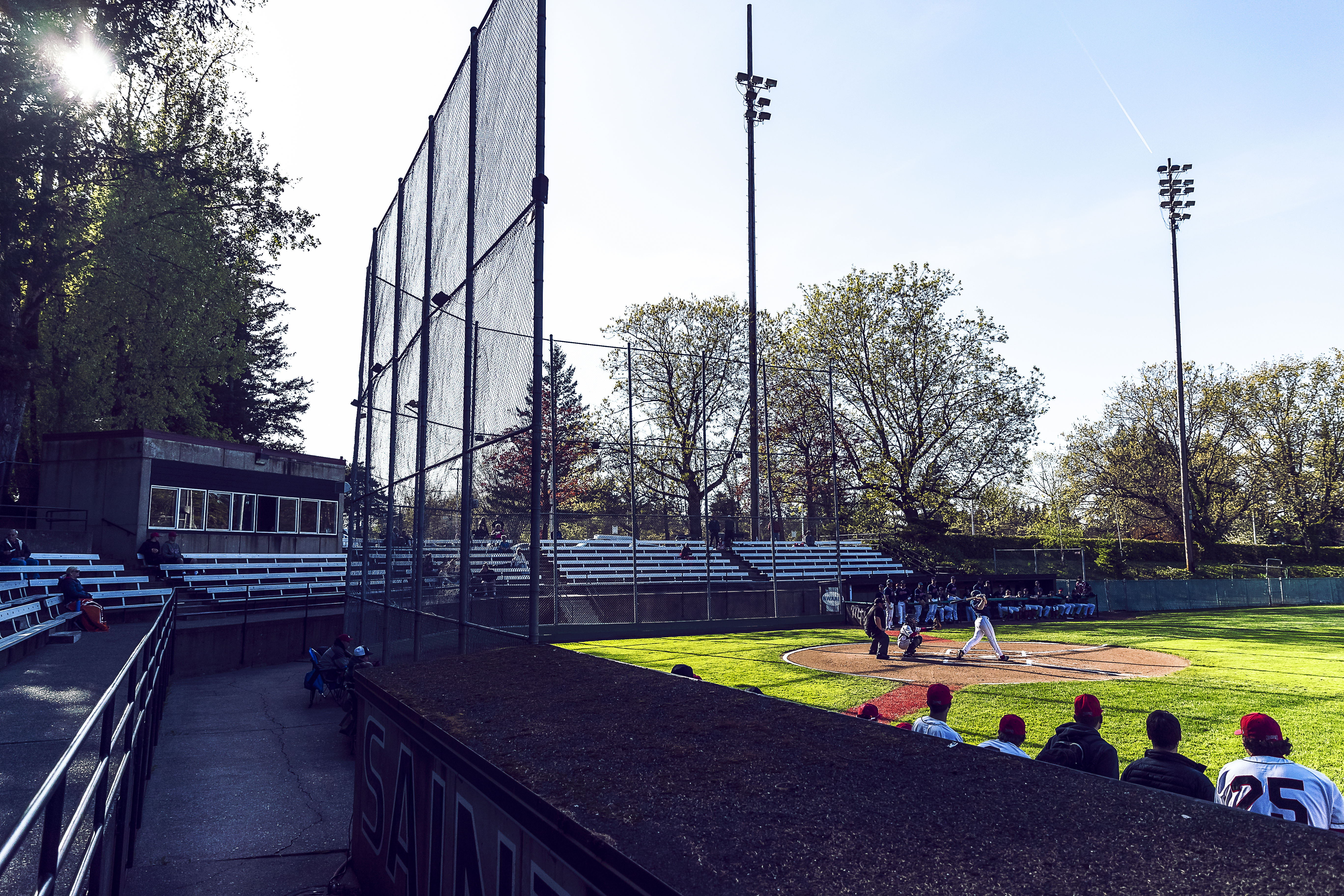 View from behind dugout of fence, bleachers, and batter swinging